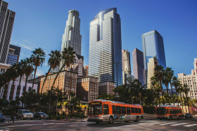 A bus drives down a street in Los Angeles, with tall buildings rising in the background.