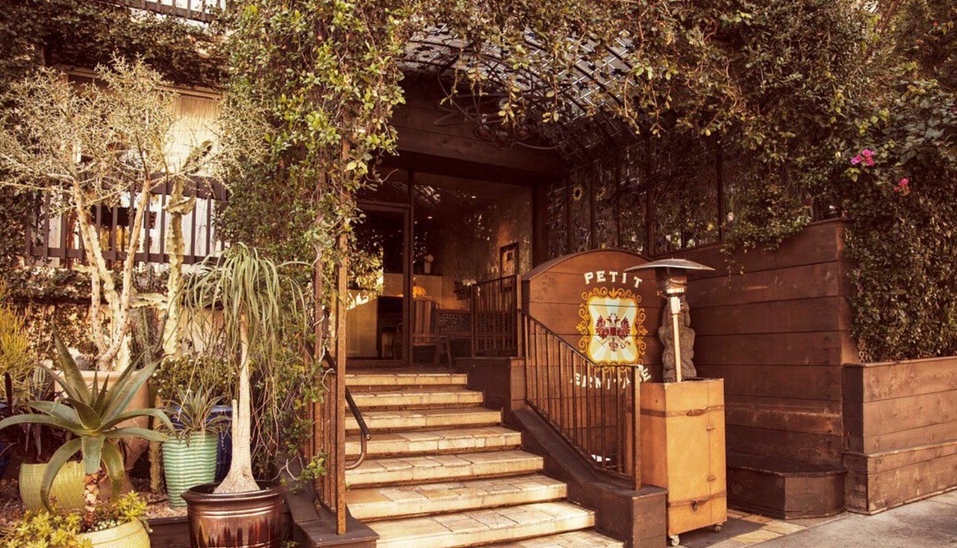 The beautiful entrance of The Petit Ermitage Hotel, covered in lush greenery.